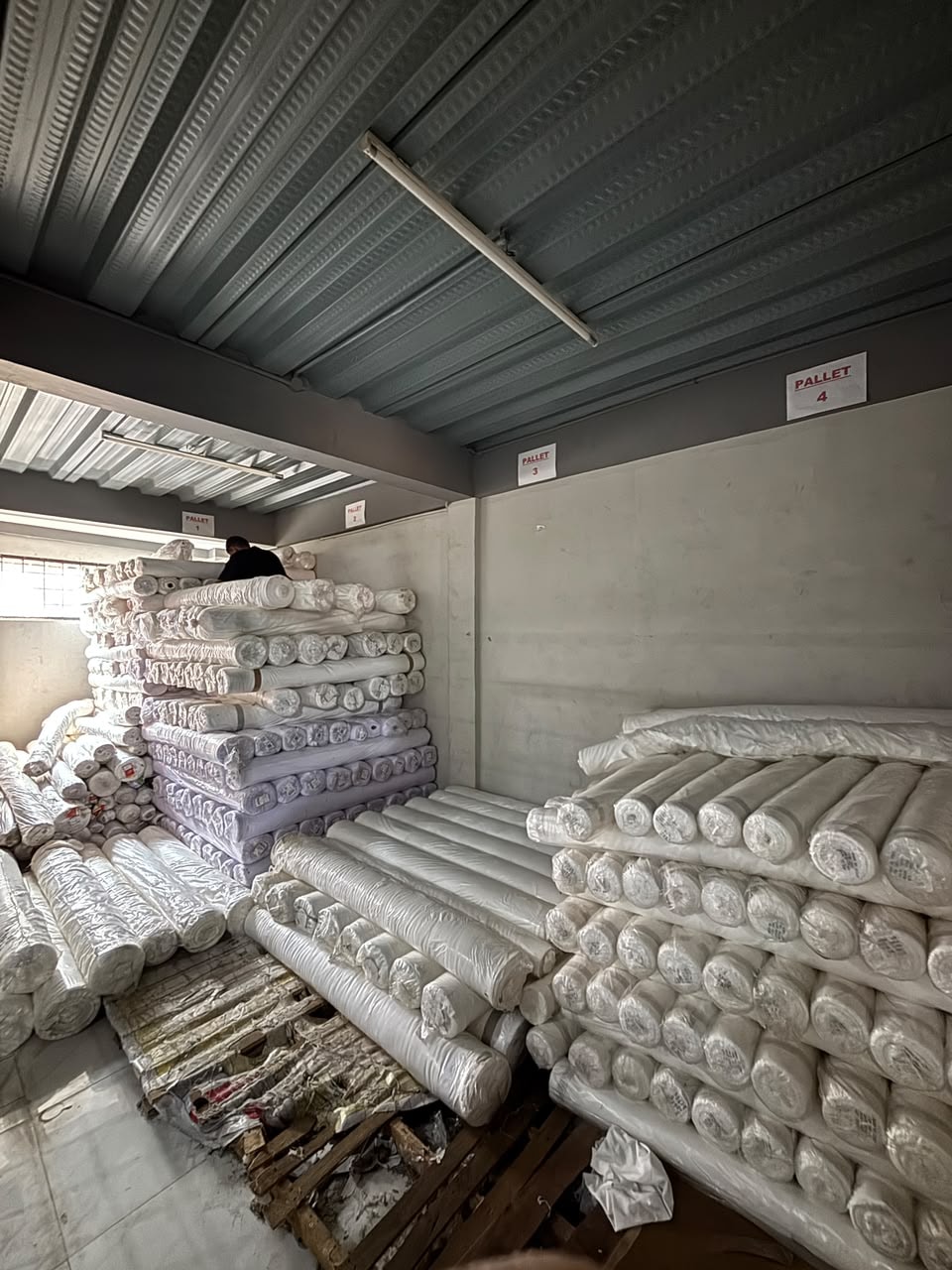 Roll kain tersusun di atas palet gudang